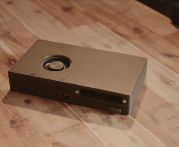 Een compacte zwarte spelconsole met een ingebouwd schijfstation, USB-poorten en een aan de bovenkant gemonteerde koelventilator, die op een houten tafel staat.