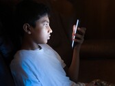Een tiener in een donkere kamer die naar een verlichte smartphone kijkt