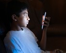 Een tiener in een donkere kamer die naar een verlichte smartphone kijkt