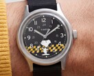 Close-up van de zwarte wijzerplaat van de Timex MK1, waarop Snoopy te zien is tegen een geel-zwart geruite achtergrond, met Arabische uurmarkeringen en lichtgevende wijzers.