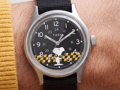 Close-up van de zwarte wijzerplaat van de Timex MK1, waarop Snoopy te zien is tegen een geel-zwart geruite achtergrond, met Arabische uurmarkeringen en lichtgevende wijzers.