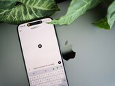 Een smartphone waarop de ChatGPT-app is geopend, rustend op een laptop naast plantenbladeren