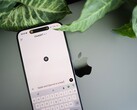 Een smartphone waarop de ChatGPT-app is geopend, rustend op een laptop naast plantenbladeren