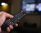 Hand die een afstandsbediening vasthoudt met een onscherpe tv op de achtergrond