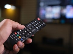 Hand die een afstandsbediening vasthoudt met een onscherpe tv op de achtergrond