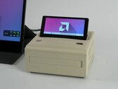 Een Ayaneo AM01S mini PC in retro-stijl met beige afwerking, voorzien van een ingebouwd opklapbaar secundair scherm waarop het Windows-bureaublad te zien is. (ETA Prime via YouTube)