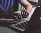 Handen die op het toetsenbord van een MacBook typen bij weinig licht, terwijl het Apple-logo oplicht