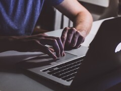 Handen die op het toetsenbord van een MacBook typen bij weinig licht, terwijl het Apple-logo oplicht