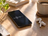 Smartphone die een audiogolfvorm weergeeft naast draadloze oordopjes en een koffiekopje op een houten bureau