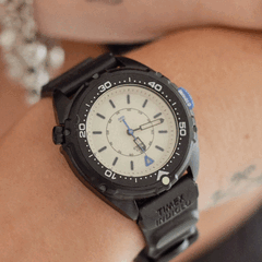 De Timex Intrepid x Dimepiece Blackout Edition heeft een zwarte roestvrijstalen kast, een crèmekleurige wijzerplaat en paarse accenten