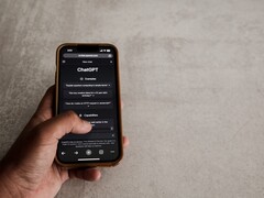 Hand die een smartphone vasthoudt waarop de ChatGPT-interface te zien is, boven een grijs stenen oppervlak