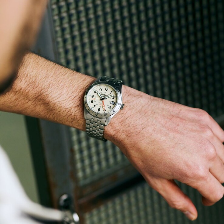 Vooraanzicht van de Seiko 5 Sports Field GMT HDB002 met een crèmekleurige wijzerplaat, een oranje GMT-wijzer, een vaste 24-uursring en een roestvrijstalen armband.