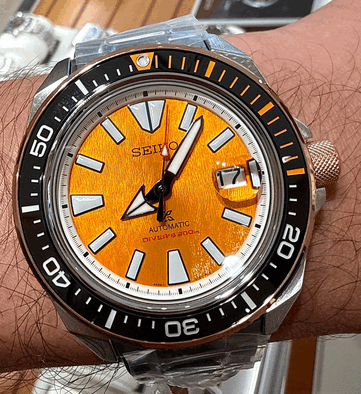 Close-up van de Seiko Prospex HBB005K1 met zijn gestructureerde amberkleurige wijzerplaat, extra grote lichtgevende uurmarkeringen, brede wijzers, datumvenster en zwarte duikring met oranje markeringen.