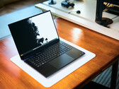 Een open, matzwarte Razer Blade 16-gaminglaptop die op een witte bureauonderlegger op een warme houten tafel staat, met een levendige zwart-witte achtergrondafbeelding.