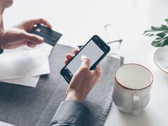 Een persoon die op een smartphone tikt terwijl hij of zij in de andere hand een bankkaart vasthoudt