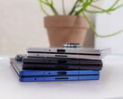 Stapel opvouwbare smartphones die het concept van de aanstaande Apple iPhone Fold voorstellen, geplaatst op een witte tafel met een potplant op de achtergrond (Afbeelding bron: Notebookcheck)