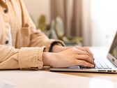 Handen die op het toetsenbord van een open laptop typen op een helder verlicht bureau