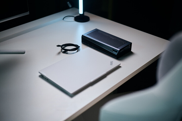 Een gesloten witte ThinkPad-laptop die naast de compacte Aorus RTX 5060 Ti AI Box eGPU en een spiraalvormige Thunderbolt-kabel op een bureau staat.