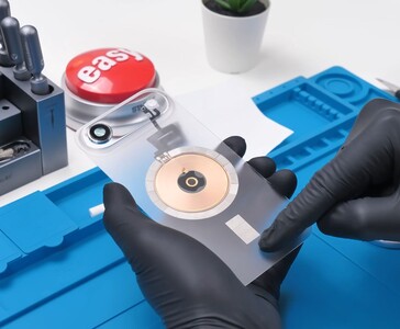 Transparant iPhone Air achterglas met zichtbare koperen draadloze oplaadspoel en cameramodule tijdens het moddingproces. (Afbeelding bron: Phone Repair Guru via YouTube)