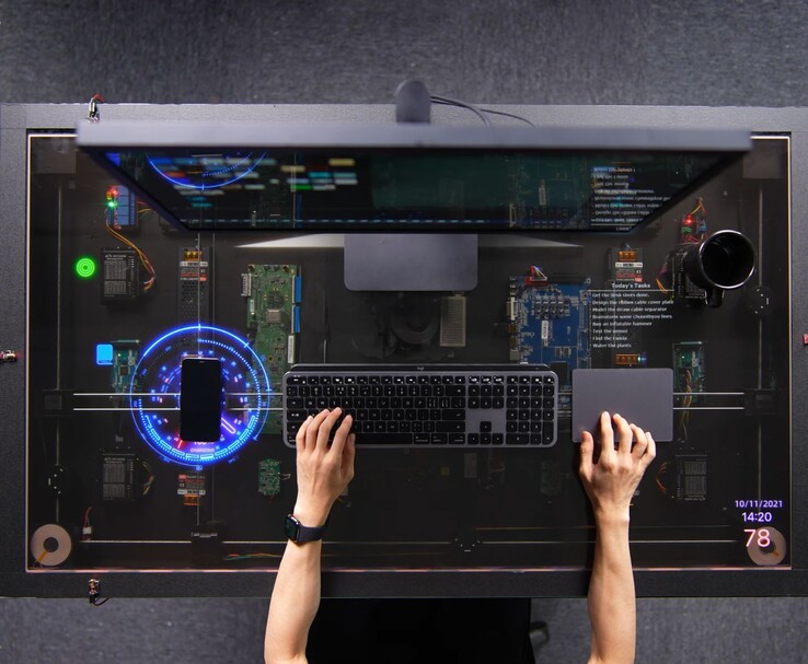 Het door AirPower geïnspireerde doe-het-zelf-bureau van HTX Studio in gebruik, met een telefoon die oplaadt op het transparante scherm naast een toetsenbord, trackpad en monitor.