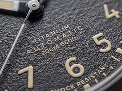 Close-up van de gestructureerde zwarte wijzerplaat van de Timex Expedition Field Post Titanium met Arabische cijfers, lichtgevende wijzers en indexen, en een datumvenster.