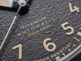 Close-up van de gestructureerde zwarte wijzerplaat van de Timex Expedition Field Post Titanium met Arabische cijfers, lichtgevende wijzers en indexen, en een datumvenster.
