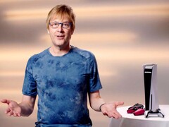 Mark Cerny tijdens een PlayStation-evenement, zittend naast een PS5-console en DualSense-controllers. (Afbeelding Bron: Sony Interactive Entertainment)