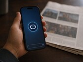 Een hand houdt een smartphone vast waarop een chatbot-pictogram te zien is; ernaast ligt een gedrukte krant.