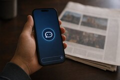 Een hand houdt een smartphone vast waarop een chatbot-pictogram te zien is; ernaast ligt een gedrukte krant.