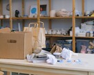 Kartonnen doos en papieren zakken op een houten tafel in een kantoor met rekken