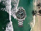 Seiko Prospex HBC001 duikershorloge met groene wijzerplaat en lunette op een achtergrond van strand en oceaan in de lucht.