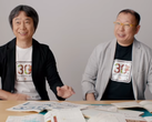 Een screengrab van Shigru Miyamoto en Tezuka Takashi in t-shirts ter ere van de 30e verjaardag van Super Mario Bros