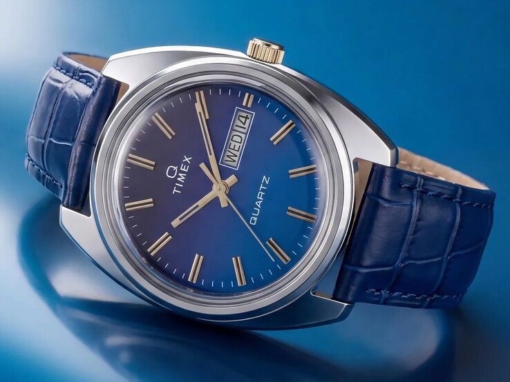 Productfoto vanuit een hoek van de Timex Q 1976 Day and Date, met nadruk op de blauwe wijzerplaat met kleurverloop, de gepolijste roestvrijstalen kast en de goudkleurige kroon.