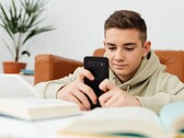 Een tiener in een hoodie die op een smartphone typt, met open schoolboeken voor zich