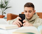 Een tiener in een hoodie die op een smartphone typt, met open schoolboeken voor zich