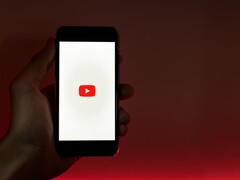 Een hand die een smartphone vasthoudt, waarop het YouTube-logo op het scherm oplicht tegen een rode achtergrond