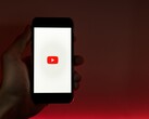 Een hand die een smartphone vasthoudt, waarop het YouTube-logo op het scherm oplicht tegen een rode achtergrond