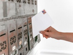 Een hand die een envelop in een rij brievenbussen steekt