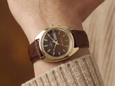 Timex Q 1978 Day and Date met een bruine fuméwijzerplaat en goudkleurige kast, getoond om een pols met een bruine leren band.