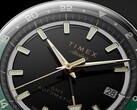 Close-up van de zwarte wijzerplaat van de Timex Atelier GMT Première M1a, met goudkleurige wijzers, lichtgevende uurmarkeringen, een datumvenster en een zwart-groene 24-uurs-GMT-ring.