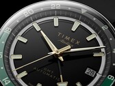 Close-up van de zwarte wijzerplaat van de Timex Atelier GMT Première M1a, met goudkleurige wijzers, lichtgevende uurmarkeringen, een datumvenster en een zwart-groene 24-uurs-GMT-ring.