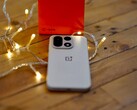 Een OnePlus 15 ligt op een houten tafel, omringd door warme lichtslingers, met op de achtergrond een felrode OnePlus-verpakking.