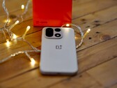 Een OnePlus 15 ligt op een houten tafel, omringd door warme lichtslingers, met op de achtergrond een felrode OnePlus-verpakking.