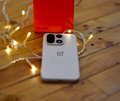 Een OnePlus 15 ligt op een houten tafel, omringd door warme lichtslingers, met op de achtergrond een felrode OnePlus-verpakking.
