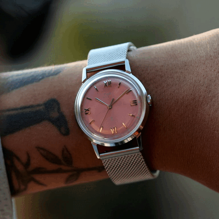 Een persoon die het Timex x Todd Snyder Marlin Mesh-horloge draagt, met een zalmkleurige wijzerplaat met sunburst-effect en een mesh-armband.