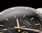 Close-up van de Timex Waterbury Heritage Automatic met zwarte wijzerplaat, waarop de gefacetteerde, lichtgevende wijzers, de uurmarkeringen, de dag- en datumweergave en de zwarte lunette te zien zijn.