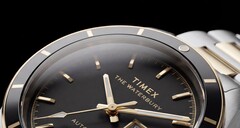 Close-up van de Timex Waterbury Heritage Automatic met zwarte wijzerplaat, waarop de gefacetteerde, lichtgevende wijzers, de uurmarkeringen, de dag- en datumweergave en de zwarte lunette te zien zijn.