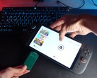 Yu van het YouTube-kanaal Better Gaming met in zijn ene hand een Nintendo Switch 2 en in zijn andere hand een open-source groene PCB-adapter, die hij in de microSD Express-sleuf van het apparaat probeert te steken (bron: Better Gaming via YouTube)
