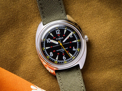 Het Timex x Bespoke Post limited-edition 36mm horloge, afgebeeld met een olijfkleurig Cordura bandje tegen een donkere mosterdkleurige achtergrond. (Afbeeldingsbron: Timex)