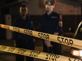 Twee politieagenten staan 's nachts achter een geel lint met de tekst Stop